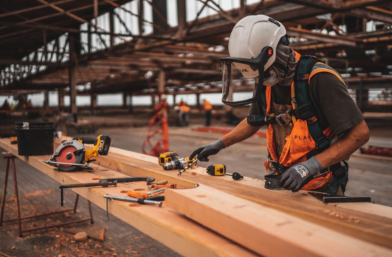 construction worker analyzing wooden planks at a workbench wearing construction helmet and gloves